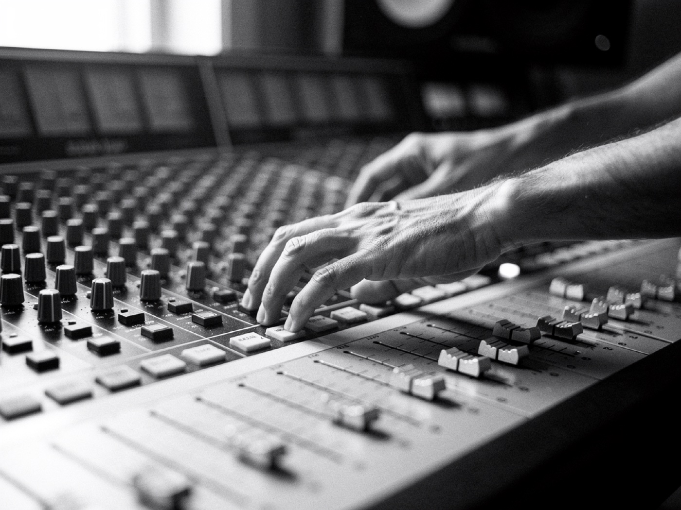 Hands on the faders of a mixing desk, shallow depth of field